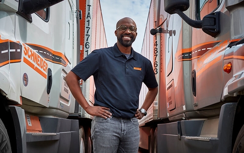 A Schneider associate stands between two company trucks.