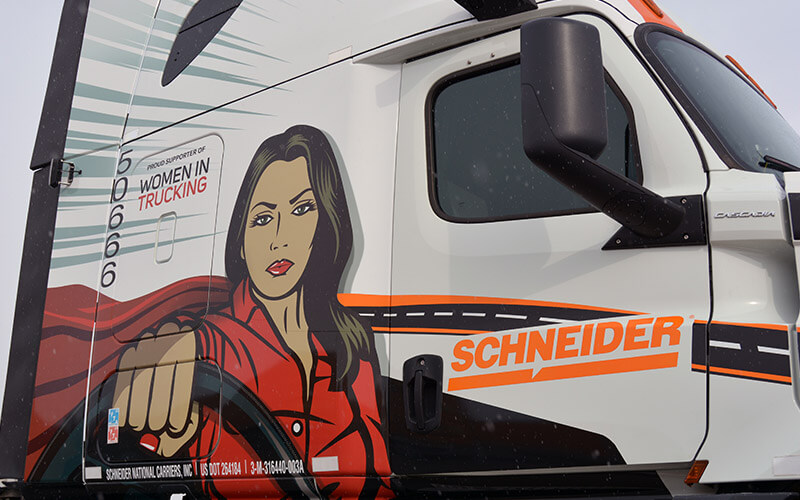KellyLynn’s truck features a caped female truck driver confidently gripping a steering wheel. Next to her is the Schneider logo and a decal that reads “Proud supporter of Women in Trucking.”