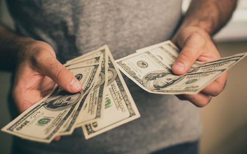 A close-up of hands holding and counting several U.S. dollar bills.