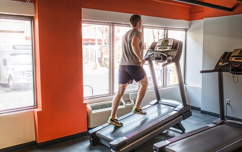 A man wearing workout attire runs on an inclined treadmill at a gym.