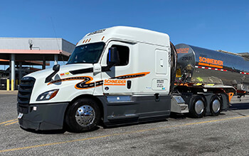 A white Schneider semi-truck hauling a chrome Schneider tanker trailer is parked at a fuel station.