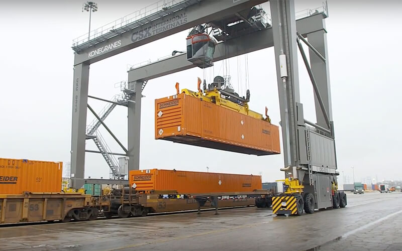 An intermodal lift loads an orange Schneider container onto a train