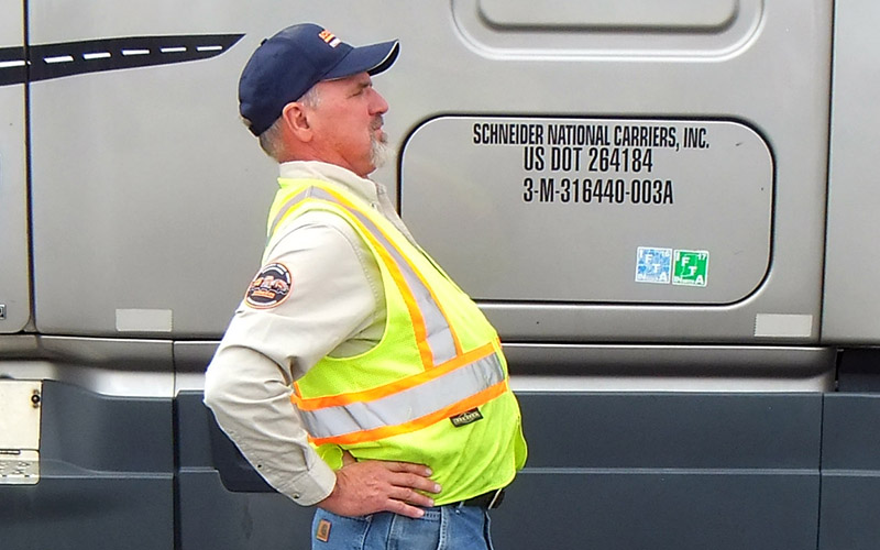 A truck driver in a safety vest stretching outside of their truck.