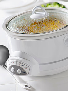 A white crock pot sits on a counter as it cooks a meal.