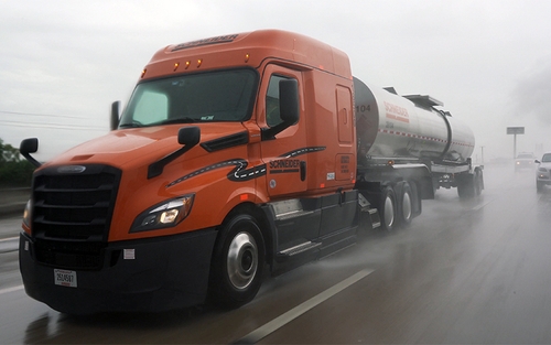 A Schneider tanker truck drives down a highway in heavy rain.