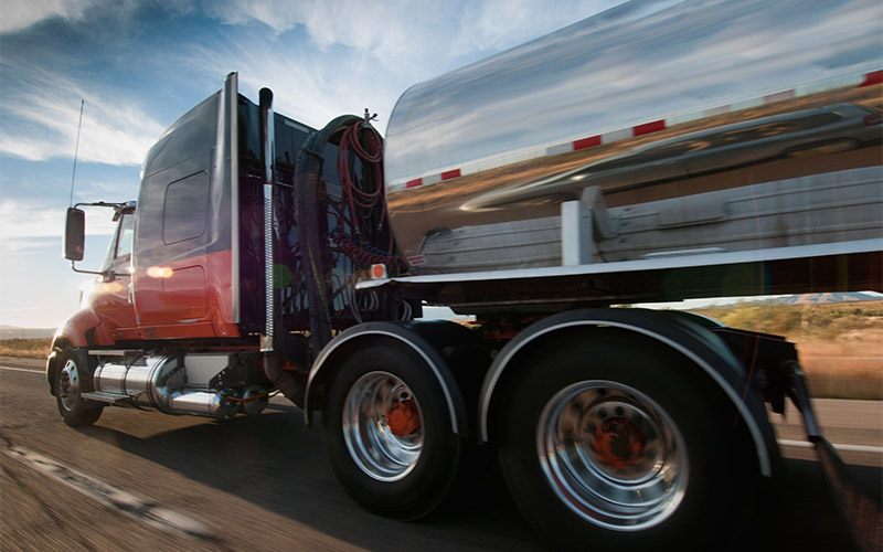 A tank truck with a silver tank driving on a highway.