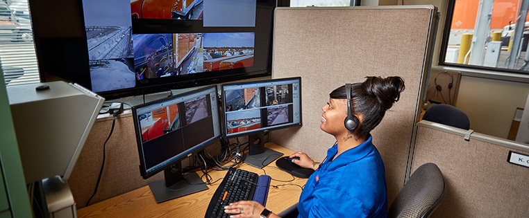 A Schneider associate monitors surveillance footage on two standard-size monitors and a large TV display at her desk.