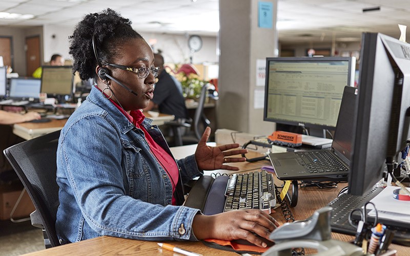 A woman talking over a headset while sitting at a desk and looking at a computer.