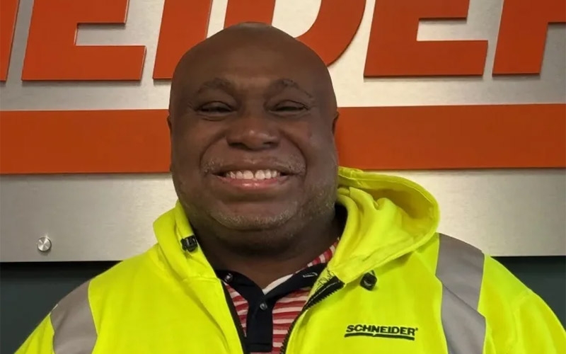 Schneider driver Mark Jackson smiling while wearing a bright yellow hi-vis safety vest.