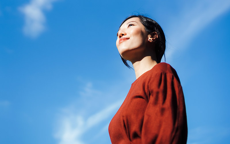 A woman standing outside looking hopefully at the sky.