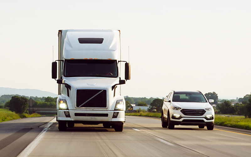 A white semi-truck driving alongside a passenger vehicle on the highway.