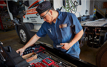A diesel technician searches for the right tool in a large and organized toolbox while performing maintenance on a Schneider truck