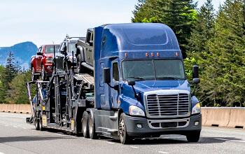 A blue semi-truck pulls a car-hauling trailer on a mountain road.
