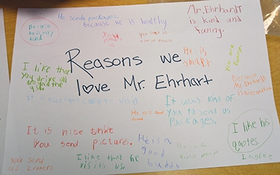 A sheet of paper titled "Reasons we love Mr. Ehrhardt" features words of praise written in crayon from students.