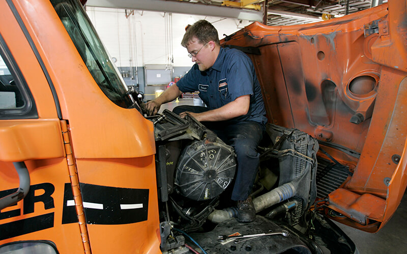 A Schneider Diesel Technician works on an engine of a Schneider truck.