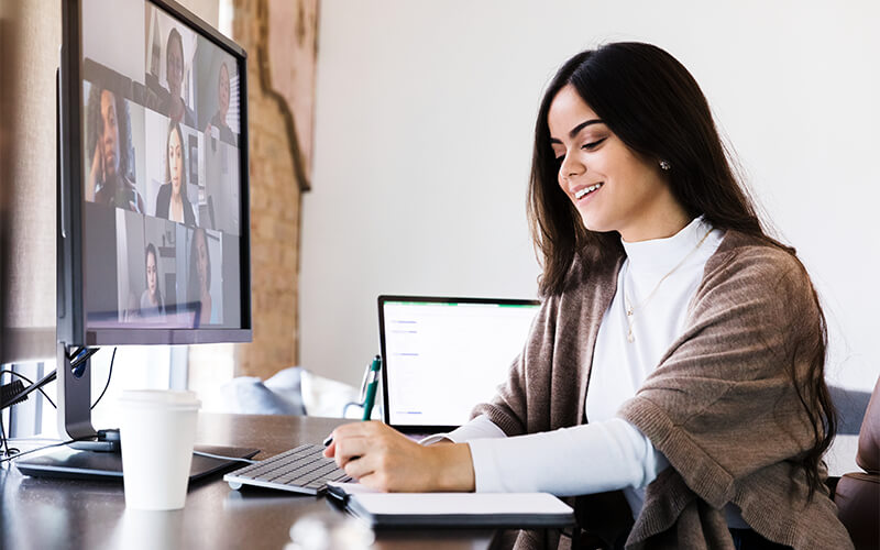 A young woman takes notes with pen and paper while in a video meeting with her work team.