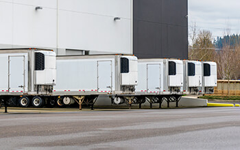 Five white drop-and-hook reefer trailers sit at the loading dock of a business, waiting to be unloaded.