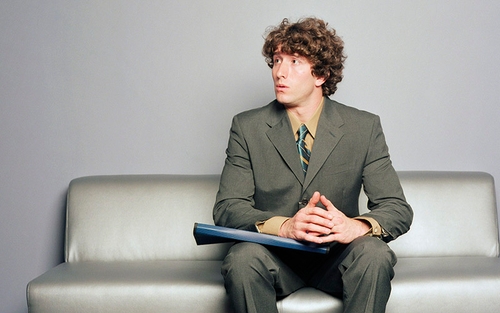 A man sitting on a couch with his hands folded in his lap.