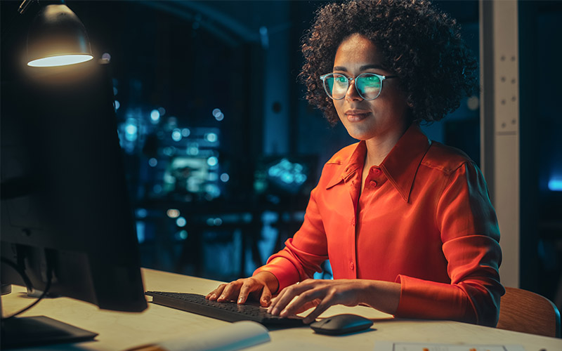 A woman sitting at a desk and working on a computer in an apartment at night.