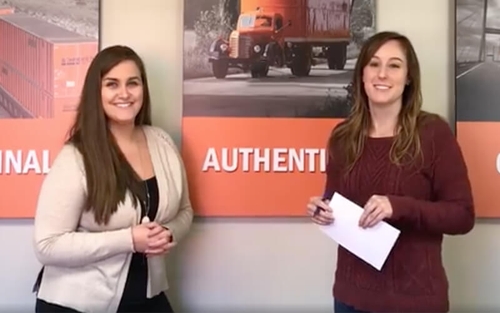 Two Schneider recruiters pose in front of a picture of an orange vintage-style company truck