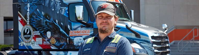 A Schneider diesel technician with military experience stands in front of Schneider's military tribute semi truck