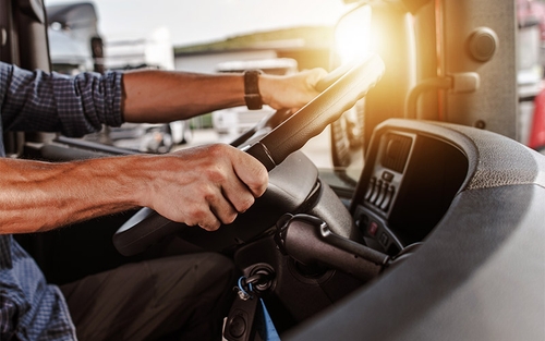 A truck driver gripping their steering wheel with two hands.
