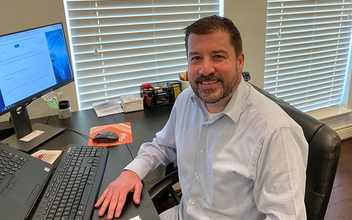 Michael Matte, wearing a white collared shirt, sits at a desk in his home office.