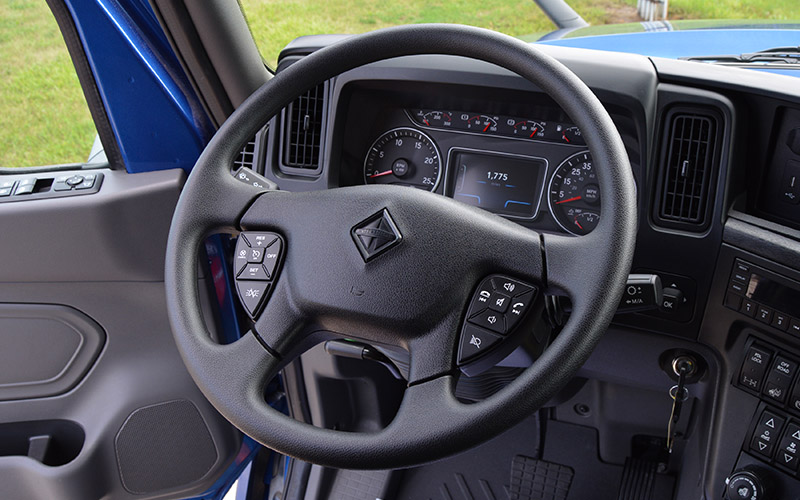 Interior view of a vehicle, focusing on the black steering wheel with embedded controls and the dashboard displaying various gauges such as speedometer, tachometer, fuel level and temperature.
