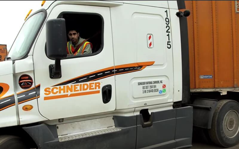 A truck driver checks his side mirrors while backing his trailer.