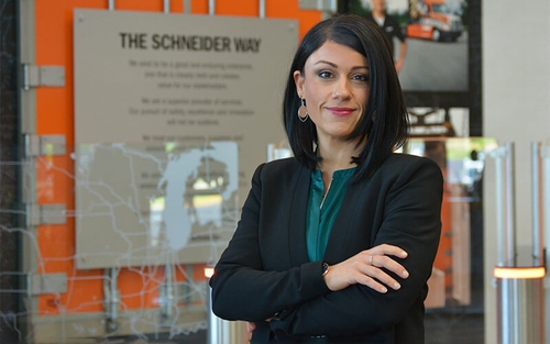 Jackie Thomas, wearing professional business clothes, poses in front of a Schneider-themed wall.