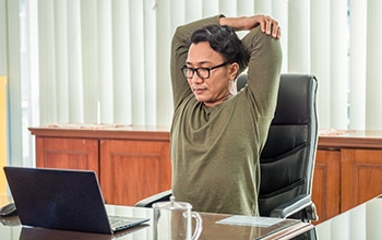 A woman stretching while sitting at her desk.