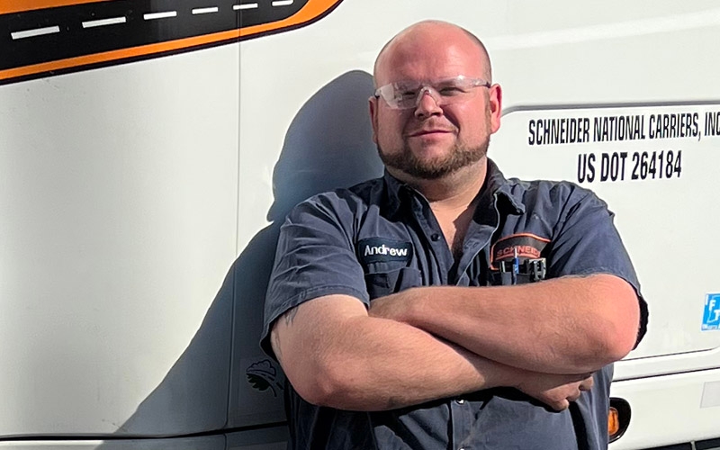 Schneider Senior Diesel Technician Andrew Mercer standing in front of a semi-truck with his arms crossed. 