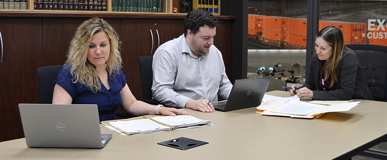 Three associates sit in the library of Schneider's Legal department, reviewing paperwork for a case.