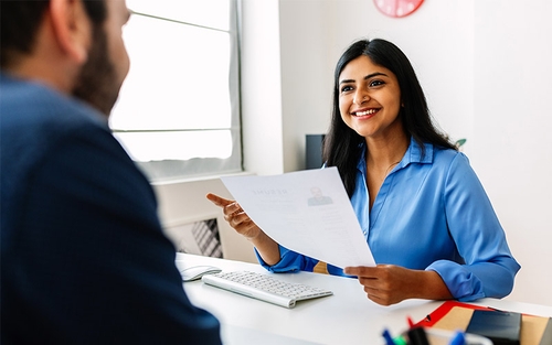 A woman talking with someone at a table and holding a resume.