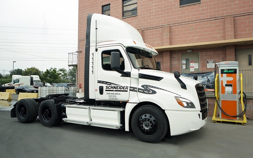 A white electric semi-tractor trailer is parked next to its charging station outside of one of Schneider’s California operating centers.