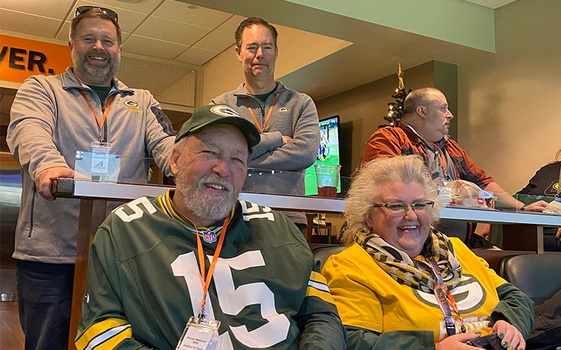 Schneider Advantage Club members wearing Green Bay Packers clothes sit in a sky box during a Packers football game.