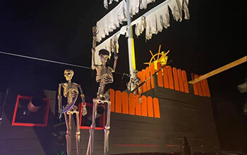 The backside of the pirate ship includes a skeleton forcing another skeleton to walk the plank, cannons, orange fencing, the captain's wheel and one of the masts.