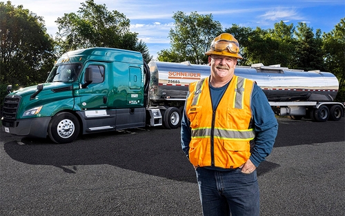 A Schneider tanker truck driver in orange PPE standing in front of a tanker trailer.