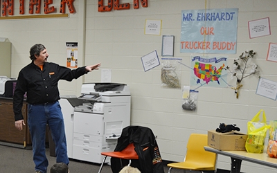 Schneider driver Rod Ehrhardt gestures to a 'Trucker Buddy' project display on the wall of an elementary school classroom.