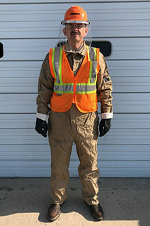 A man wears a flame retardant suit, gloves, a safety vest and a hard hat with a visor.