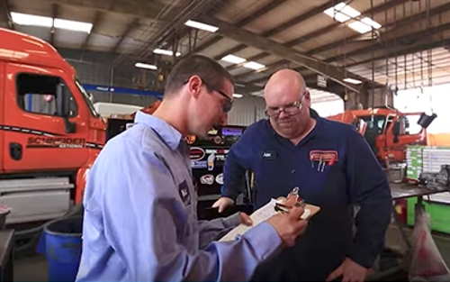 Two Schneider diesel technicians go over information on a clipboard on the shop floor.