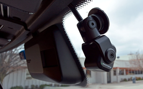A black forward-facing SmartDrive camera is attached to the dash of a semi truck.