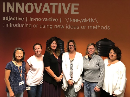 Schneider women associates in technology gather under a wall featuring the dictionary definition "Innovative - introducing or using new ideas or methods."