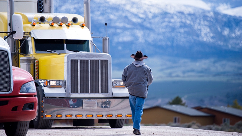 A truck driver walks to his truck while taking in the views of a nearby mountain range.