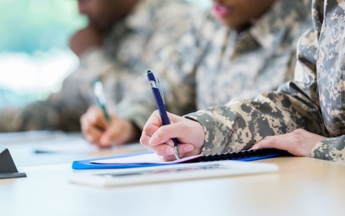 Three uniformed military service members sit at a table and fill out paperwork.