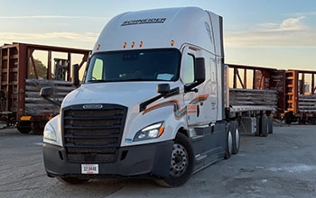 A white Schneider tractor carrying a partially loaded flatbed trailer.
