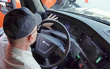 Driving Instructor Brett waves his hand in front of the odometer of a 2021 Freightliner Cascadia semi-truck.