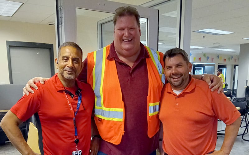 Three Schneider drivers and associates pose together during a driver appreciation celebration, with one person wearing a high-visibility safety vest.