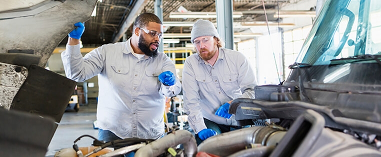Two diesel technicians looking at the engine of a semi truck inside a maintenance shop.