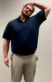 A physical therapist demonstrates stretching his neck by placing his left hand on the right side of his head and pulling his head to the right.